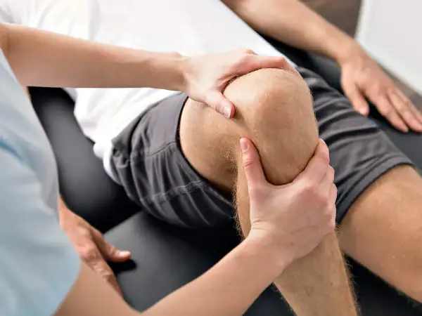 Physiotherapeut untersucht das Knie eines Mannes, um Probleme mit dem hinteren Kreuzband zu identifizieren.